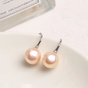 Macro view of light pink freshwater pearl earrings with silver metal hooks on a white bowl