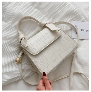Detailed close-up of cream crocodile pattern handbag with gold hardware and knotted handle