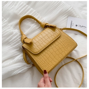 Detail of yellow crocodile embossed leather handbag with knotted handle and shoulder strap