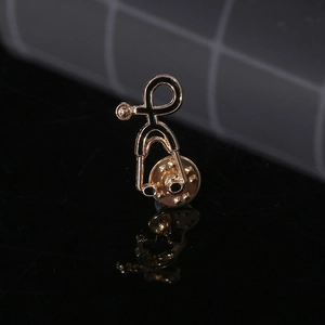 Macro shot of gold and black stethoscope enamel pin with reflections on dark mirror surface