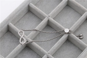 Adjustable stainless steel infinity bracelet with pavé diamonds on a grey jewelry tray