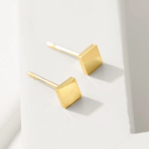 Close-up of golden square stud earrings on a white minimalist geometric background