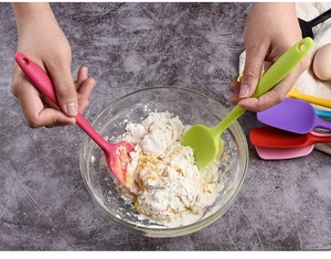 Action shot of hands using colorful silicone spatulas to mix dough in a glass bowl