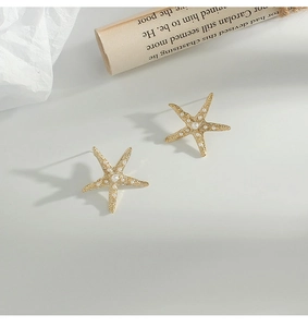 Macro detail of golden starfish stud earrings with pearls on elegant vintage background