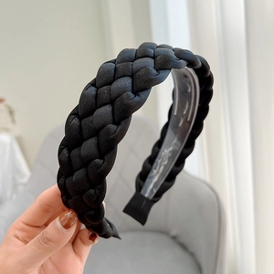 Close-up of a hand holding a black braided fabric headband with a clear plastic tooth grip