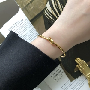 Detail of a polished 18K gold plated knot cuff bracelet worn on a wrist for styling
