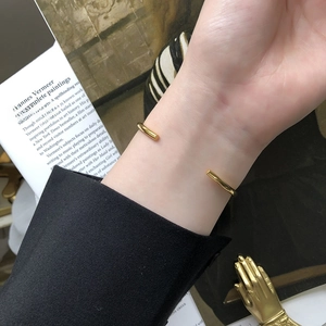 Detail of minimalist gold-plated knot cuff bracelet on wrist with artistic background