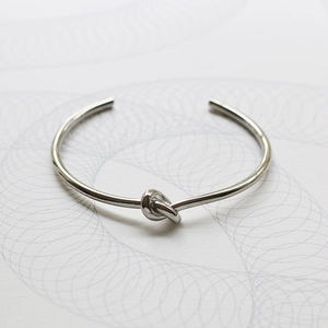 Close-up detail of silver-tone polished metal knot cuff bracelet with a minimalist design