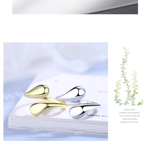 Dettaglio di anelli a goccia oro e argento su supporto bianco con decoro verde