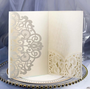 Detailed laser-cut lace wedding invitation cover in cream pearl paper on a gold tray