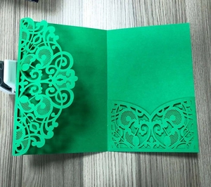 Close-up of green laser-cut lace invitation card with intricate patterns on wood desk
