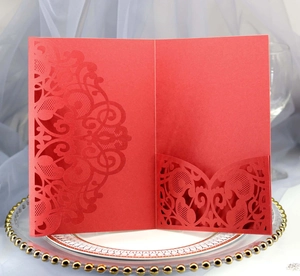 Detailed laser-cut pattern on red lace wedding invitation placed on a decorative gold plate