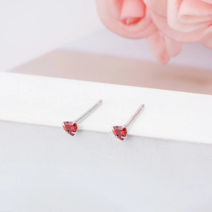 Detailed macro shot of red heart-shaped stud earrings on white pedestal