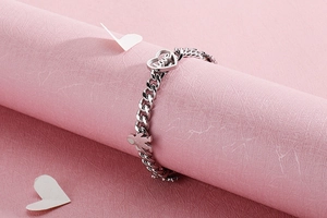 Detail of silver Cuban chain bracelet featuring hollow heart and figure charms