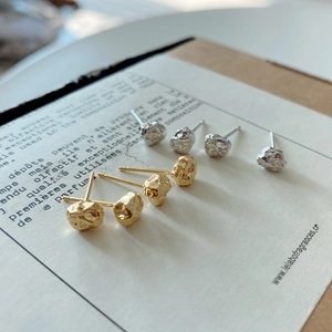 Close-up of silver and gold irregular lava rock earrings on vintage paper packaging
