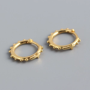 Détail de boucles d'oreilles créoles croix dorées avec texture perlée et style épuré