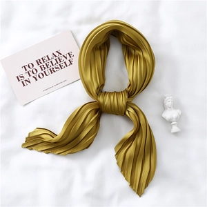 Detail of a mustard yellow pleated satin scarf with silky texture and artistic styling