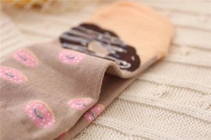 Macro detail of cotton socks featuring a cute pink donut pattern on soft brown knit