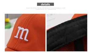 Detail of orange kids baseball cap with M embroidery and cotton twill fabric texture