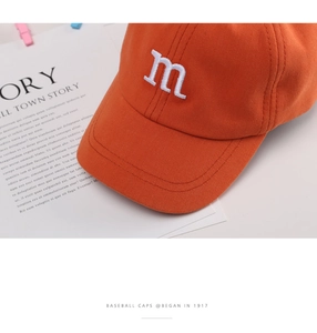 Close-up of fine white M letter embroidery on orange cotton twill baseball cap