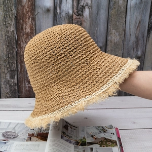 Detail of a khaki hand-woven straw hat with fringe edges on a wooden table setup