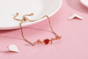 Detail of rose gold heartbeat bracelet with red heart pendant on pink background