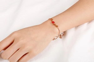 Detailed view of rose gold heart bracelet with red pendant on model's wrist