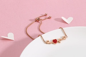 Detail of rose gold bracelet with red heart diamond and heartbeat line on a white edge