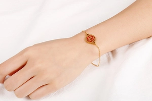 Gros plan d'un bracelet rose dorée avec émail rouge porté au poignet d'une femme