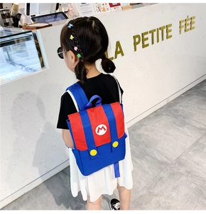 Toddler modeling a red and blue backpack with M letter design in a shop setting