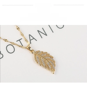 Macro detail of gold feather pendant with sparkling zircon inlay on leaf texture