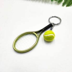 Close-up of a mini tennis racket and yellow ball keychain with metallic green finish