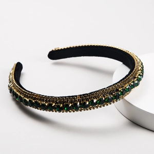 Baroque style velvet headband with green rhinestones on a minimalist white stone stand