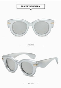 Detail view of silvery oval sunglasses with golden streamline accents and light grey lenses