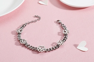 Detailaufnahme eines silbernen Pfotenabdruck-Armbands aus Edelstahl auf rosa Hintergrund