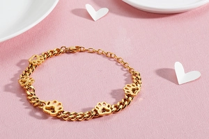 Detailansicht eines goldenen Armbands mit Hundepfoten-Anhänger auf rosa Hintergrund