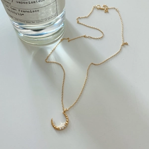 Detailed macro view of gold crescent moon necklace pendant with embedded zircons on white base