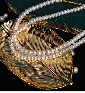Close-up of white freshwater pearl necklace on golden and green leaf-shaped trays