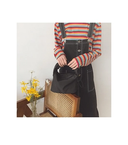 Gros plan d'un sac baguette noir minimaliste tenu par un mannequin en décor naturel