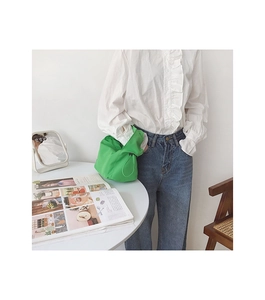 Détail d'un sac à cordon en nylon vert vif avec plis, tenu par un mannequin en extérieur