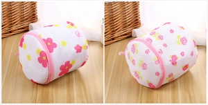 Close-up of cylinder mesh laundry bags with floral prints and pink zippers on a wood surface