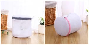 Close-up of cylindrical laundry mesh bag with grey and pink zippers on wooden surface