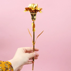Detailed close-up of a golden metal carnation held by hand against a pink background