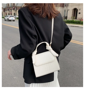 Detail view of white crocodile pattern handbag with twisted handle and long shoulder strap