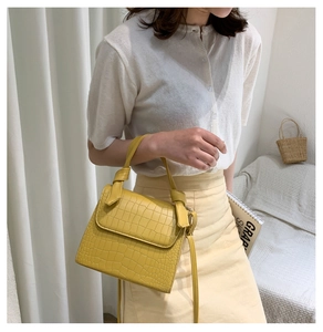 Detail of yellow crocodile embossed texture and knot handle on a mini square handbag