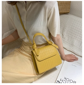Detail view of a yellow crocodile-pattern mini handbag worn by a model in a lifestyle setting