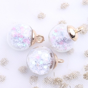 Macro detail of clear glass ball pendant with pink and white star sequins and gold loop