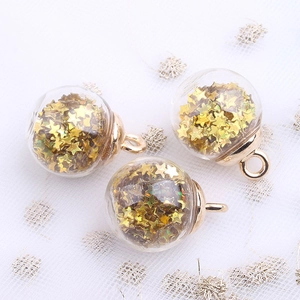 Three clear glass ball charms filled with gold star sequins on white lace texture