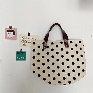 Polka dot canvas tote bag with brown leather handles and rivets on a white background