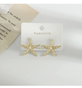 Detailed view of gold starfish earrings with faux pearls on a minimalist white card